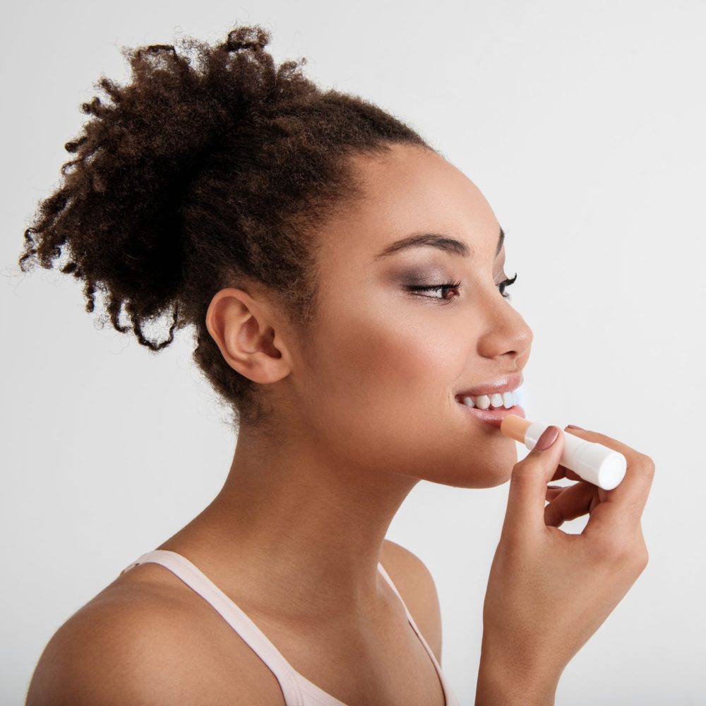 Daily makeup. Side view profile of young lady painting her lips with satisfaction. Copy space in right side. Isolated on background