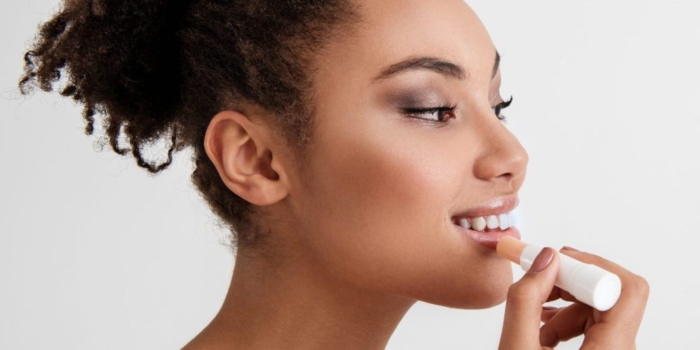 Daily makeup. Side view profile of young lady painting her lips with satisfaction. Copy space in right side. Isolated on background